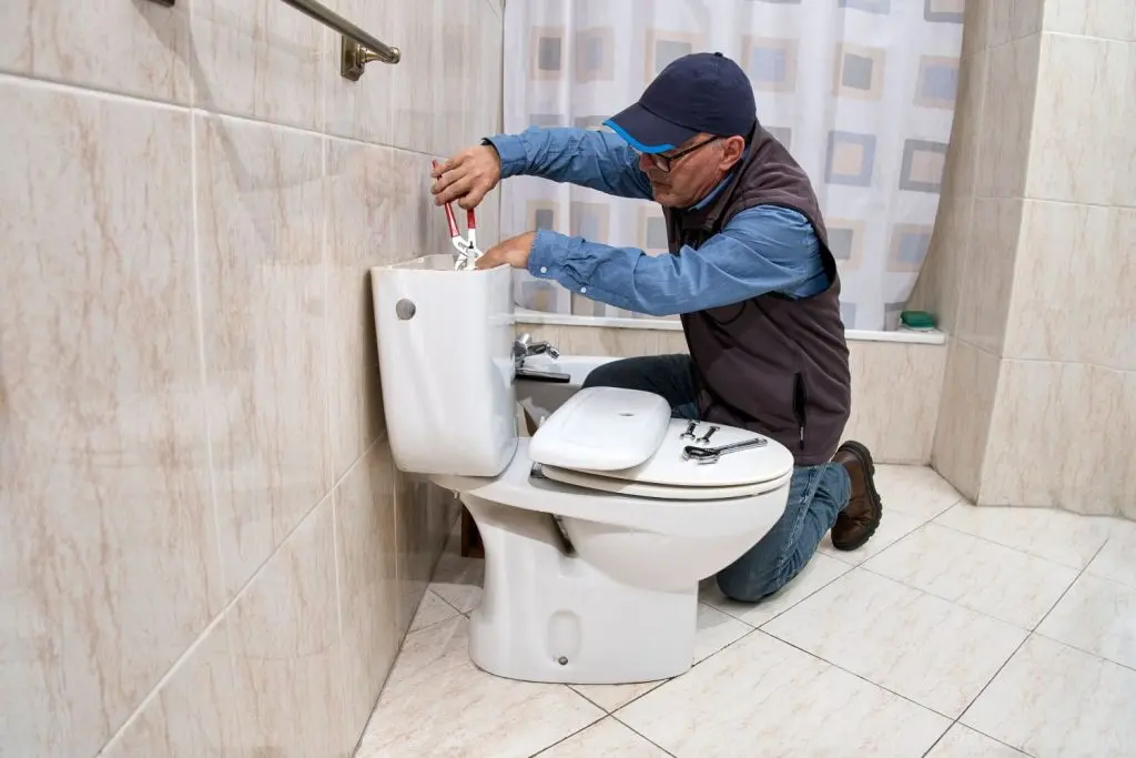 Plumber repairing components in a toilet's tank.